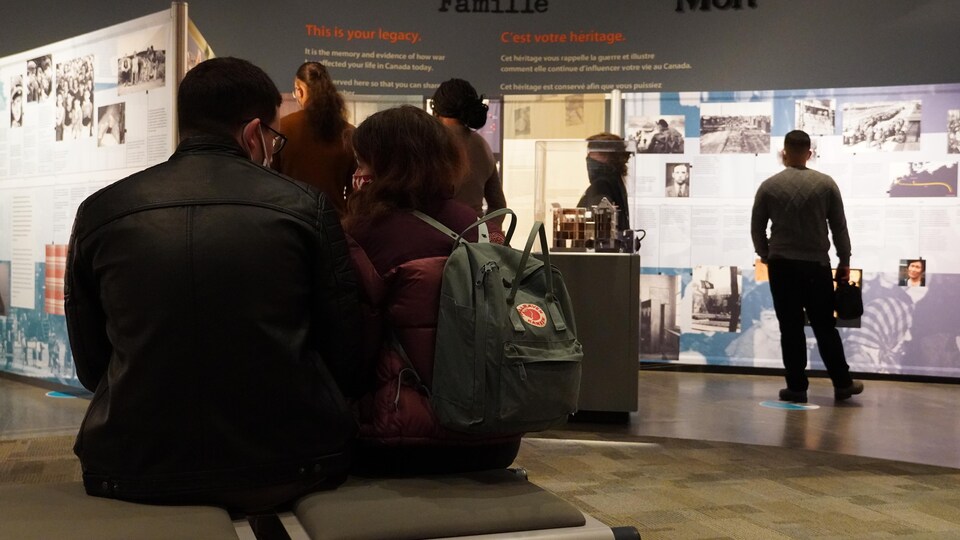 Deux personnes assises devant des panneaux d'une exposition.
