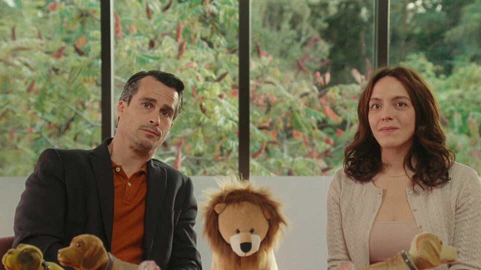 Un homme et une femme assis l'un à côté de l'autre; une peluche de lion se trouve entre eux.