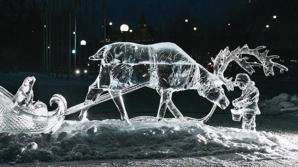 Une sculpture de glace d'une personne qui tend un sceau à un renne qui tire un traineau.