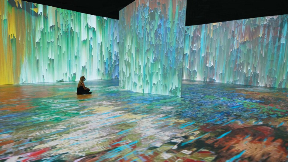 Une fille assise devant une projection d'un tableau de Van Gogh projeté sur un grand mur.
