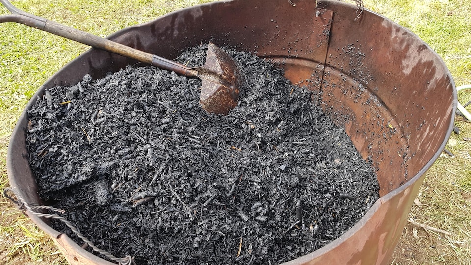 Du biocharbon dans un cylindre métallique et une pelle.