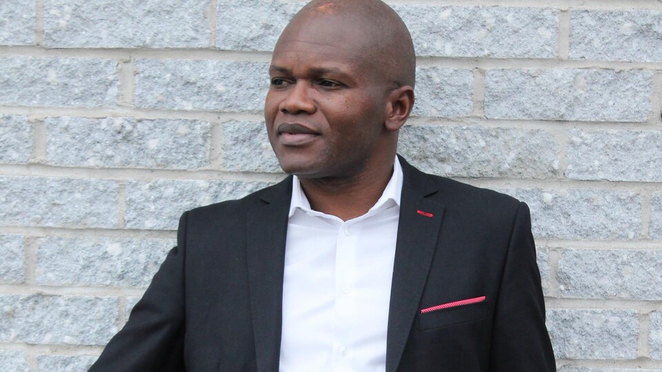 Blaise Ndala appuyé sur un mur de brique.