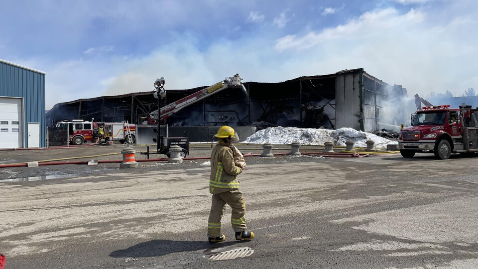 Un pompier marche devant la scène d'un feu. Un entrepôt a été complètement ravagé par les flammes.