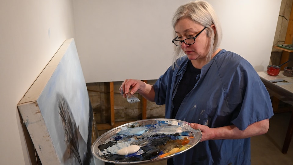 Brigitte Dion, tablette de peinture à la main, s'apprête à appliquer de la peinture sur sa toile.