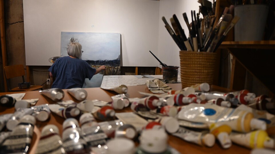 Devant l'artiste qui peint, une table avec des tubes de peintures