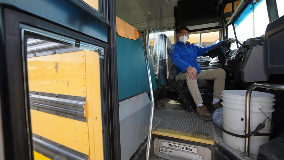 Un conducteur de bus scolaire est installé au volant et est équipé d'un couvre-visage.