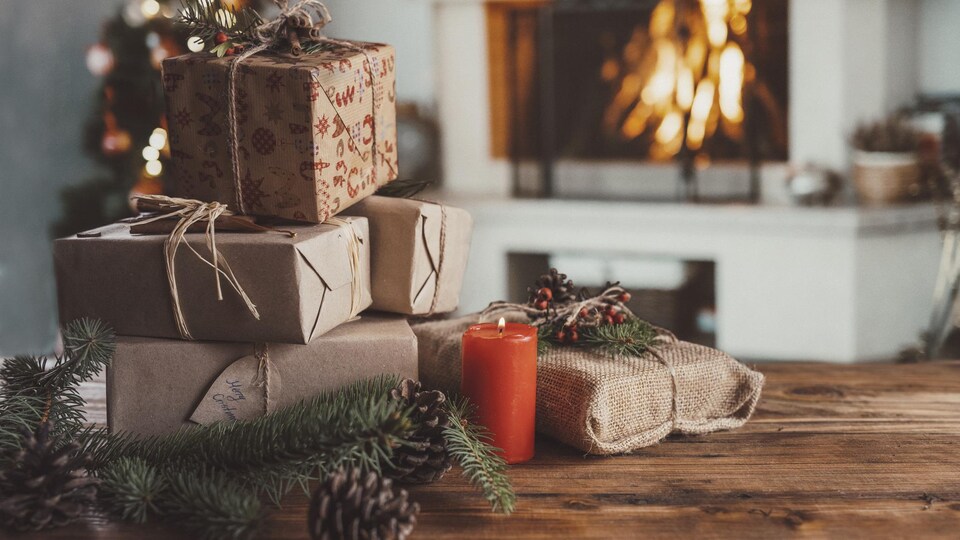 Une pile de cadeaux de Noël sur une table en bois devant une décoration de Noël.