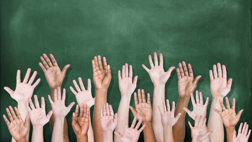 Plusieurs bras et mains tendues vers le haut devant un tableau d'école.