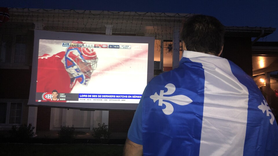 Un homme portant un drapeau du Québec regarde un match du Canadien.