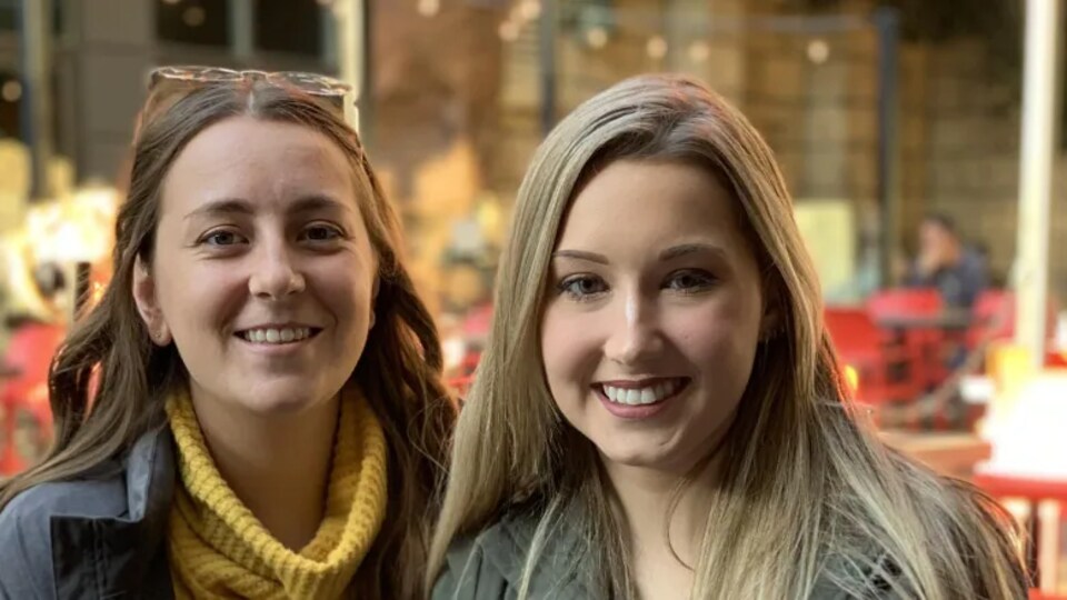 Deux jeunes femmes sourient à la caméra.
