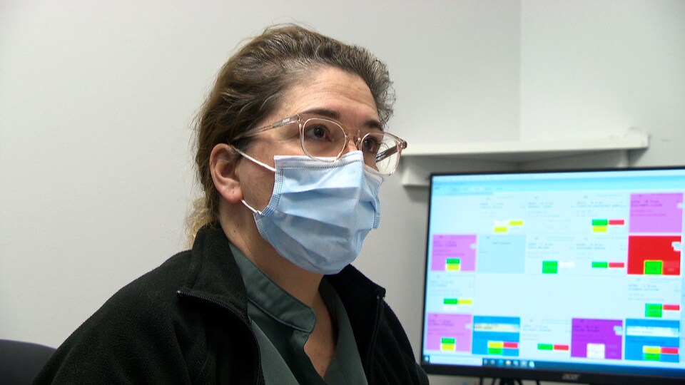 Catherine April porte un masque chirurgical et est assise devant un écran d'ordinateur.