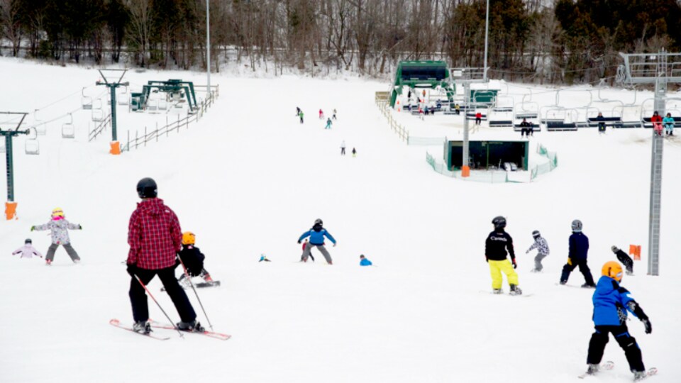 Des gens dévalent une piste de ski au milieu de remontées mécaniques.