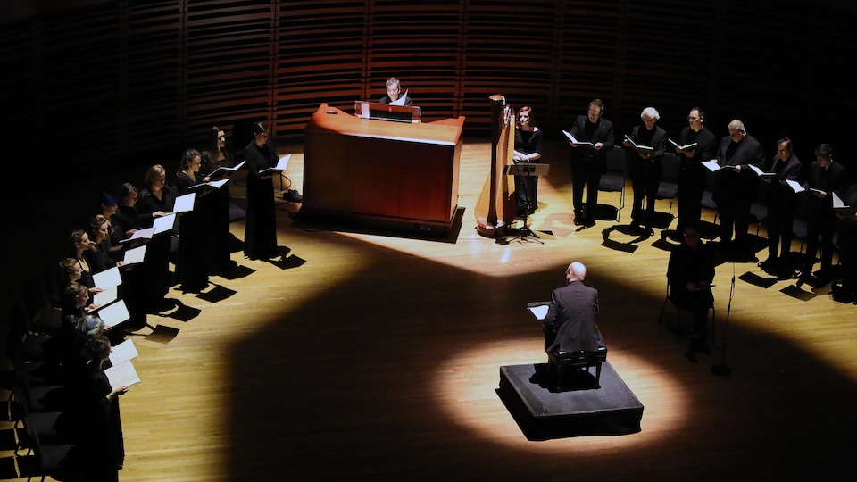 Un chœur avec un piano, une harpe et un chef d'orchestre sont illuminés dans la pénombre.