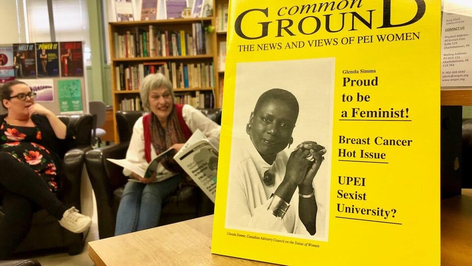 Une image de la couverture du magazine avec une photo d’une femme noire. Deux femmes sont assises au fond de la salle. Plusieurs livres se retrouvent sur des étagères encore plus au fond.