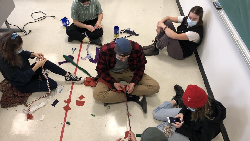 Des étudiants tressent des tapis, assis par terre.