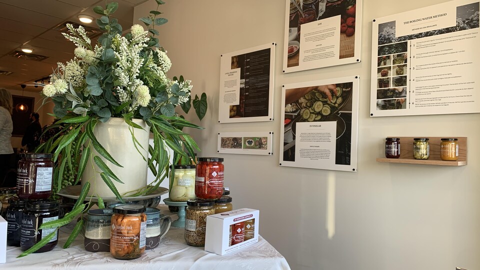 Des panneaux sont accrochés au mur pour décrire le processus de confection des conserves. Sur la table, des conserves confectionnées par Twisted Fork sont présentées.  
