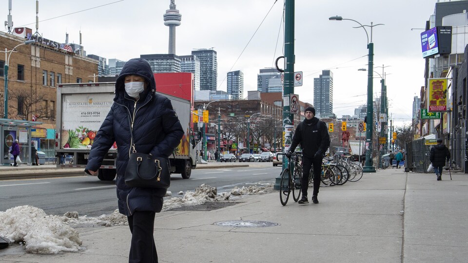 Une femme portant un masque sanitaire marche dans une rue du quartier chinois de Toronto.
