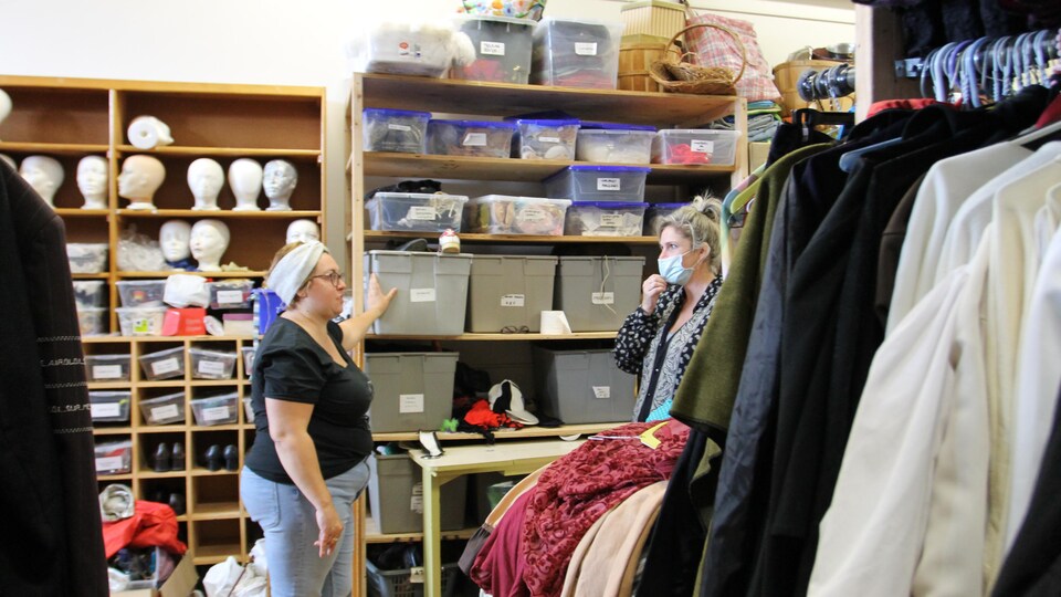 Une dame parle avec une autre à travers des dizaines de costumes et de bacs contenant des accessoires théâtraux.