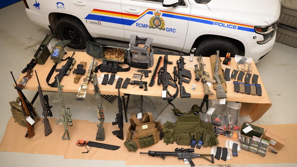 De nombreuses armes sur des tables, devant un véhicule de la GRC.
