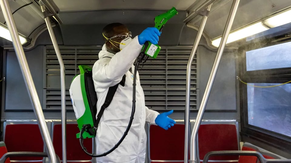 Un employé sous contrat avec la CTT montre comment il désinfecte un autobus au moyen d'un pulvérisateur.