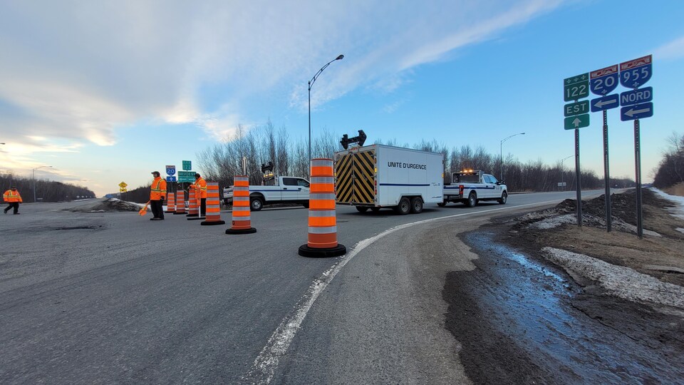 Une route fermée. Des cônes, des signaleurs et un véhicule "Unité d'urgence" barrent le chemin.