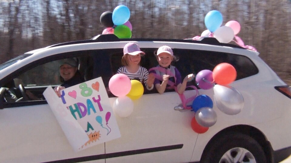 Deux petites filles sortent leur tête d'une voiture décorée avec plein de ballons d'anniversaire.