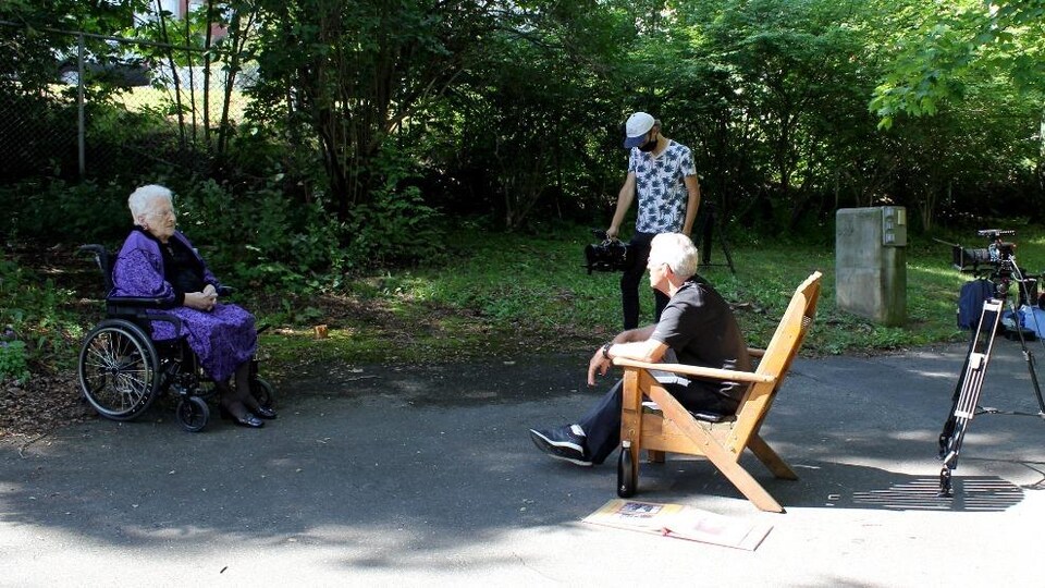 Assise dans un fauteuil roulant, Yvonne Delorme parle à un homme sur un plateau de tournage.