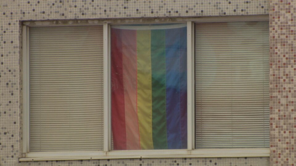 Un drapeau aux couleurs de la communauté LGBTQ est affiché dans une fenêtre.
