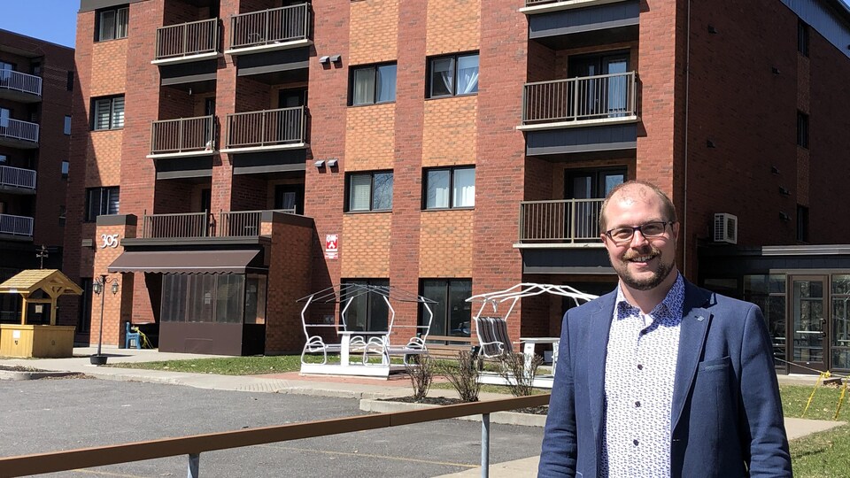 David Bélanger sourit devant un immeuble à logements.