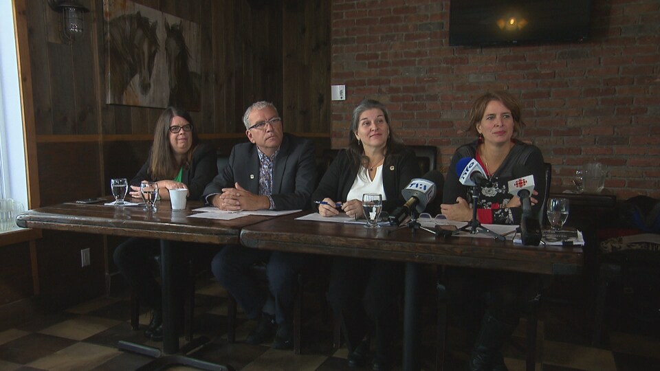 Les quatre conseillers sont assis à une table de conférence de presse.