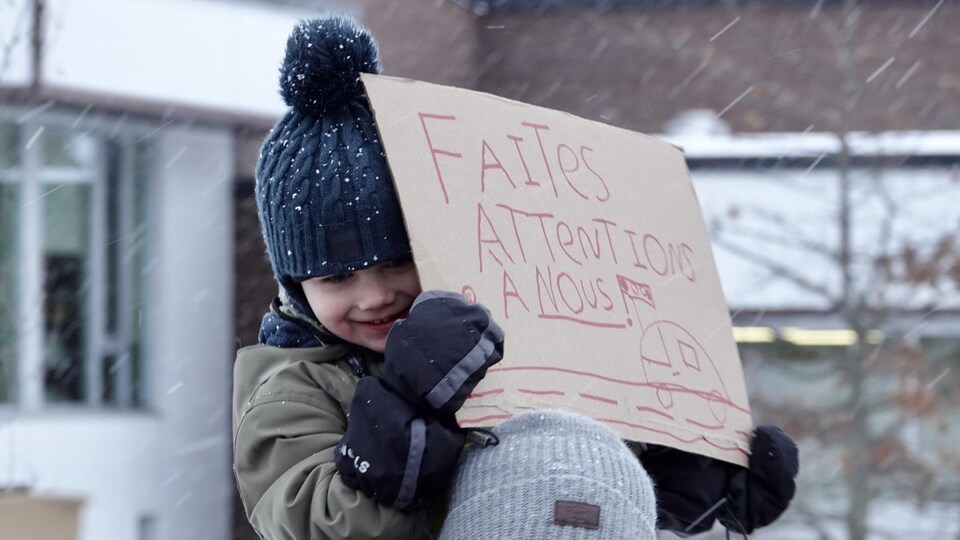 Un jeune garçon tient une pancarte sur laquelle il est écrit de faire attention à eux.