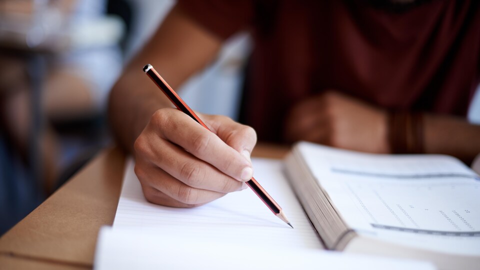 Un étudiant assis a un bureau écrit un examen.