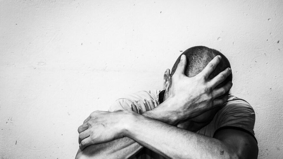 Un homme assis par terre, la tête appuyée dans sa main.