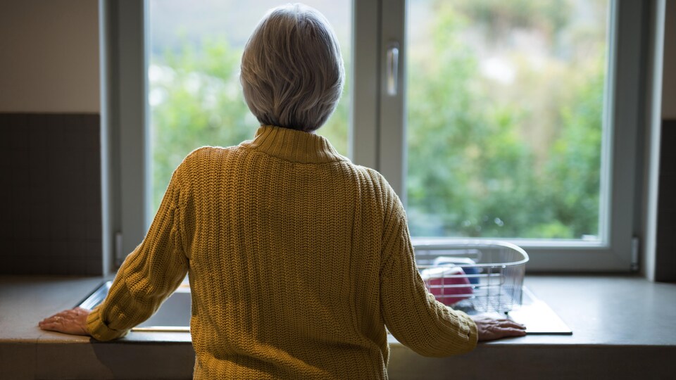 Une femme, près d'un lavabo, regarde à l'extérieur.