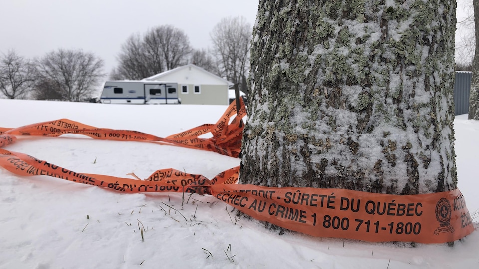 Un ruban de scène de crime entoure un arbre près d'une maison.