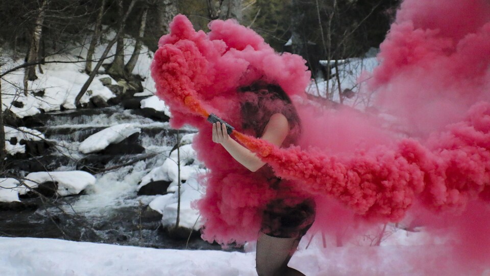 Une femme qui tient un fumigène rouge dans un décor hivernal.
