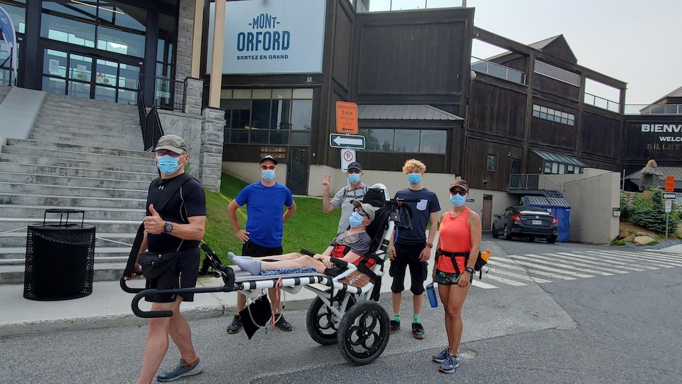 Fernand Courchesne et quatre autres bénévoles transportent un fauteuil roulant tout-terrain pour monter la montagne.