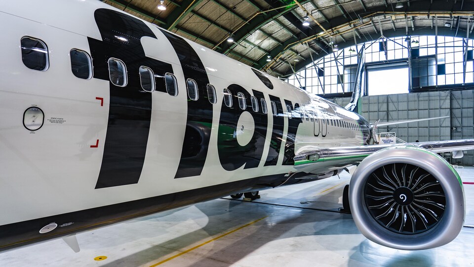 Plan moyen du côté de l'avion et l'un des réacteur. Le nom de la compagnie est écrit en grosses lettres noires. L'avion est à l'intérieur d'un hangar.