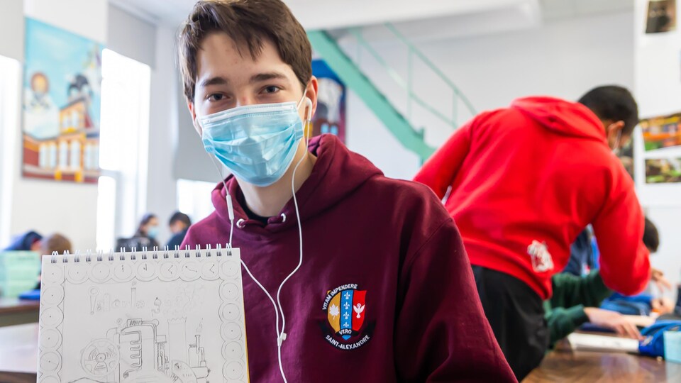 Un jeune homme avec un masque qui tient un cahier avec un dessin sur une page.