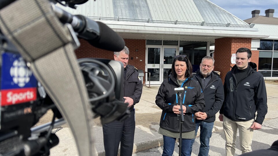 La mairesse de Gatineau accompagnée de trois hommes , devant un micro, devant un bâtiment municipal.