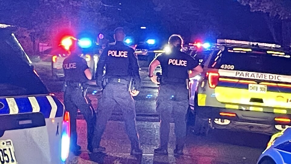 Des policiers en uniforme se tiennent entre un véhicule de police et un véhicule paramédical.