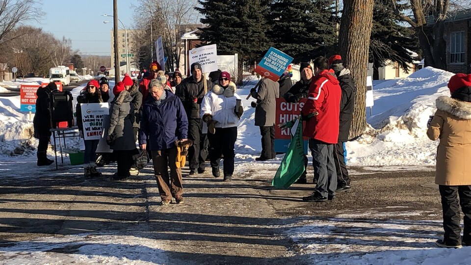 Des manifestants opposés à la politique dans l'éducation du gouvernement Ford marchent dans une rue enneigée de Thunder Bay.
