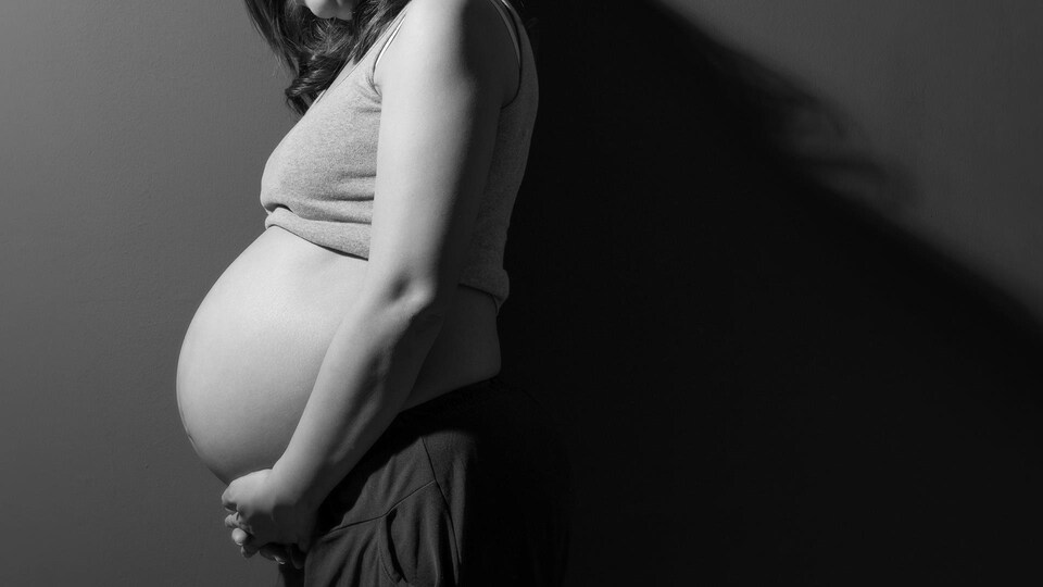Une femme enceinte qui se tient le vendre dans un éclairage sombre.