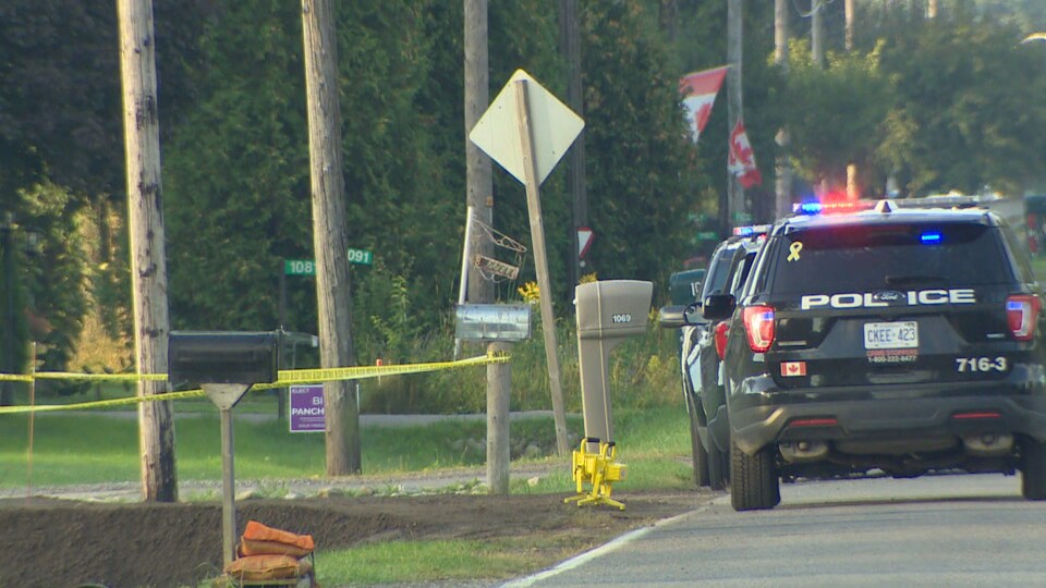 Des véhicules de police stationnés devant l'entrée d'un chemin.