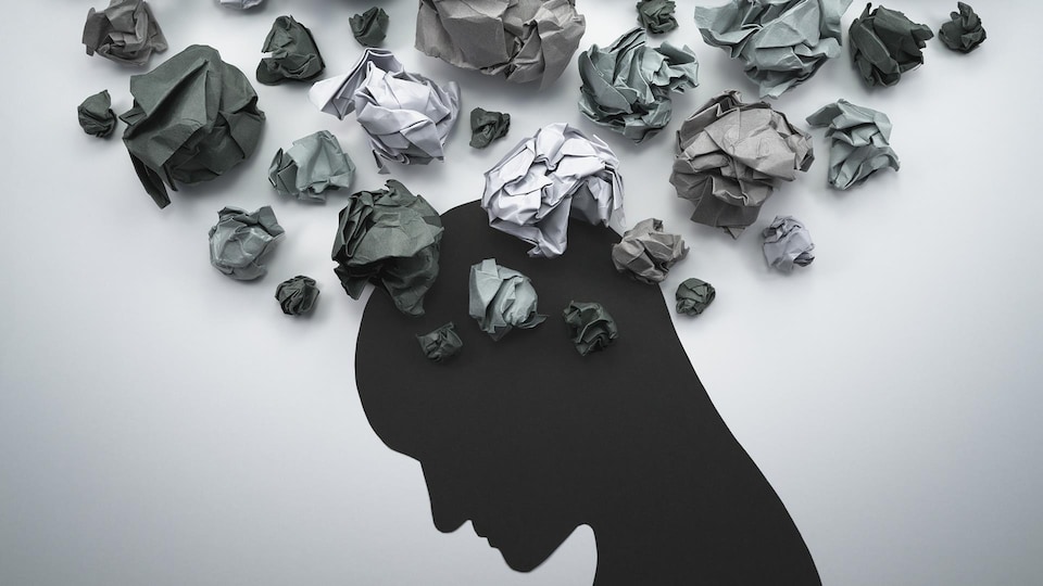 Illustration en papier d'une tête qui a des pensées troubles représentées par des boules de papier froissées.