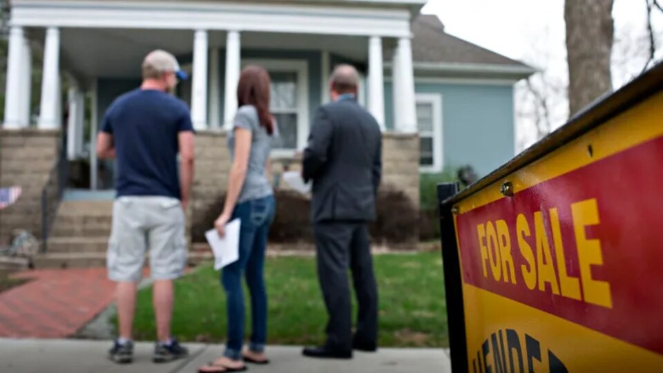 Des gens regardent la devanture d'une maison en vente.