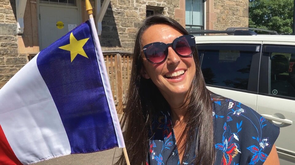 La député Isabelle Thériault lève un drapeau acadien en souriant, le 14 août 2020.