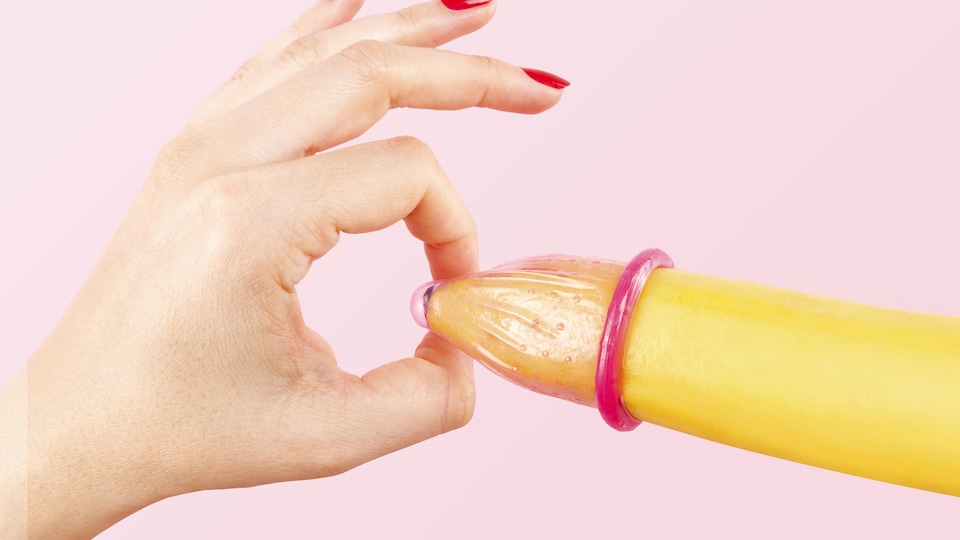 Une main de femme avec des ongles rouges met un condom sur une banane. La grande majorité des cas rapportés de syphilis, soit 95 %, sont des hommes.