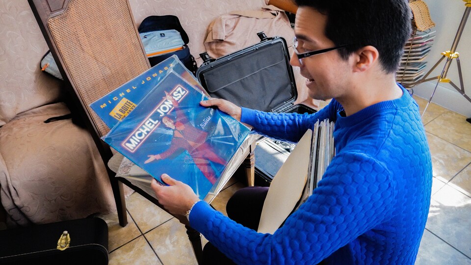 Un homme avec un grand sourire qui tient des pochettes de disques vinyle dans ses mains.
