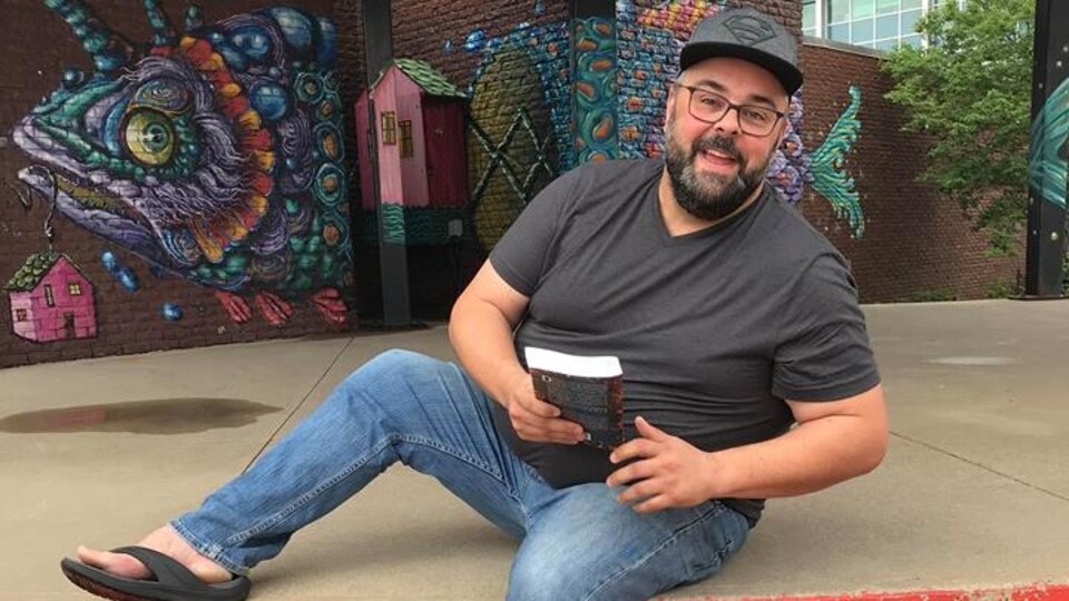 Jean-Sébastien Levesque est assis sur une scène extérieure tenant un livre.